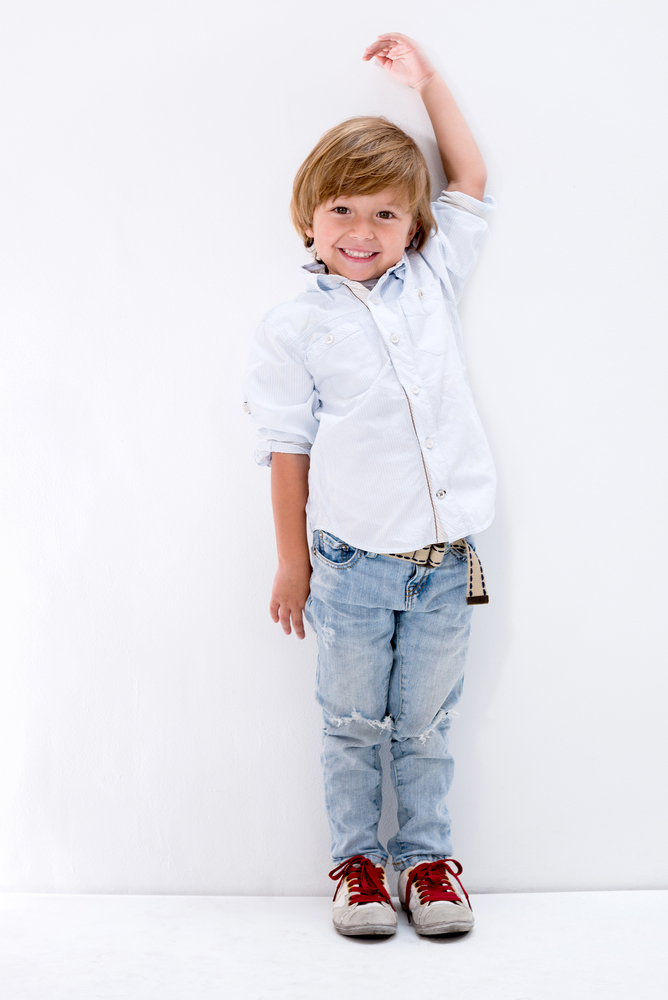 Happy boy growing up to be tall leaning against the wall